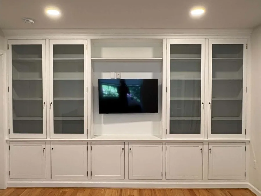 White built-in entertainment center with glass-front cabinets installed in a living room