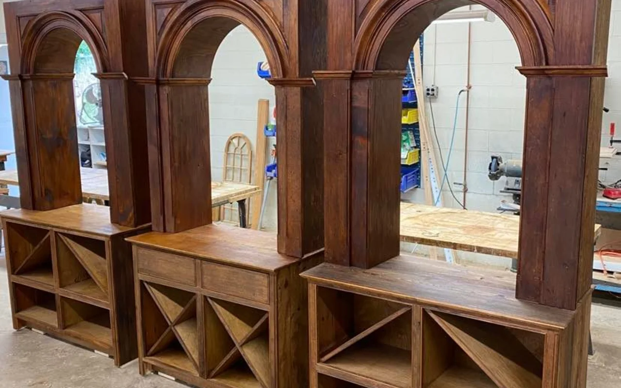 Three finished arched reclaimed-wood cabinets with X-shelving standing in a woodworking shop