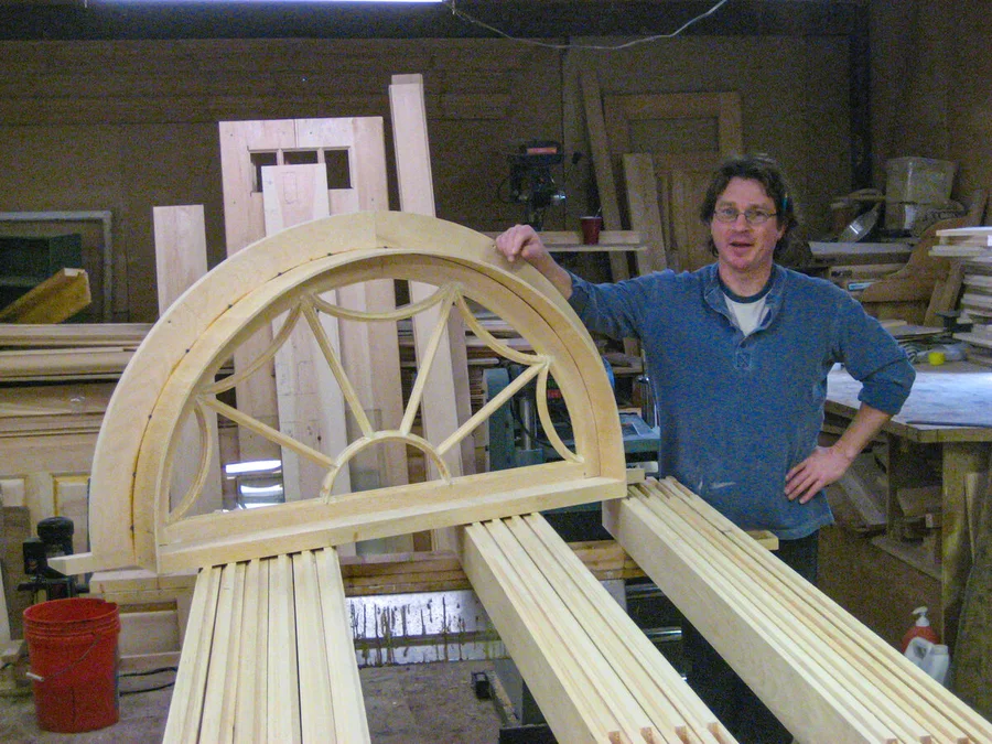 Michael Britten in his workshop holding a finished arched fanlight window he built